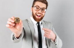 A cheerful businessman holding a Bitcoin and pointing at it with his other hand.