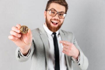 A cheerful businessman holding a Bitcoin and pointing at it with his other hand.
